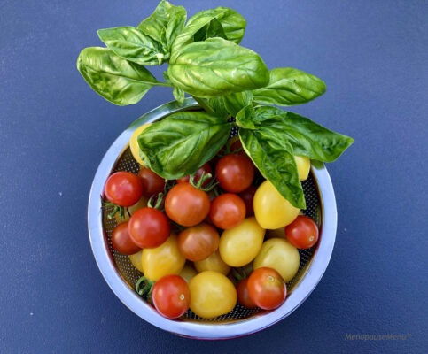 A bowl of yellow and red cherry tomatoes, with a few sprigs of basil